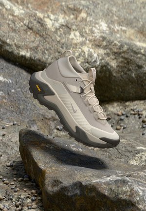 Beige og grå vandresko med Vibram-sål, der svæver over klippefyldt terræn.