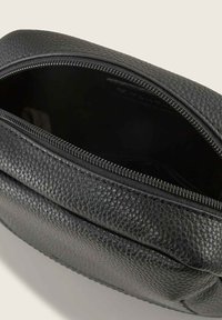 Pochette in pelle nera testurizzata con una cerniera parzialmente aperta che mostra un interno vuoto su uno sfondo chiaro.