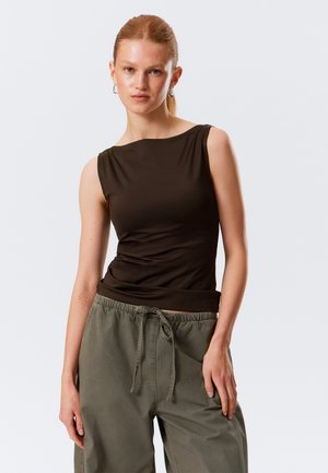 Bruine mouwloze top met een ronde halslijn en een geplooide taille, gecombineerd met losse olijfgroene broeken met een elastische tailleband.