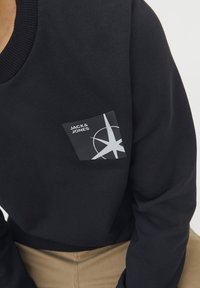 Felpa nera in cotone, con collo a costine e una toppa rettangolare con un design geometrico in bianco.