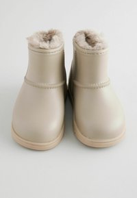 Beige imiteret læderankelstøvler med blød pelsfoer, runde tæer og en glat overflade. Inkluderer syning detaljer omkring overdelen.