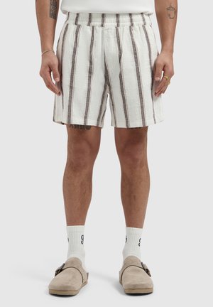 Men’s white shorts with brown vertical stripes, elastic waistband, paired with white socks and beige slip-on shoes.