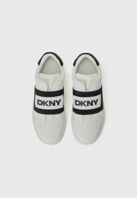 Le sneakers bianche DKNY presentano un collo imbottito, una fascia elastica nera con logo, una superficie liscia, una punta arrotondata e un design minimalista.