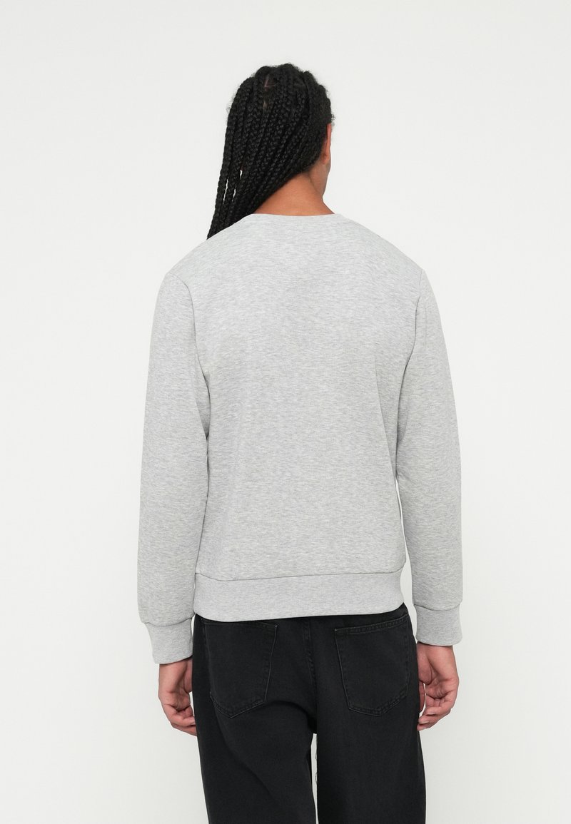 Sudadera gris hecha de una mezcla de algodón, con cuello redondo, puños acanalados y un ajuste relajado. Llevada con jeans negros.