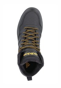 Zapatilla deportiva negra con un acabado de cuero suave, detalles en dorado, cordones anaranjados texturizados y un collar suave y peludo. Presenta un logotipo en la lengüeta.