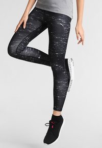 Mustat legginssit, joissa on teksturoitu kuvio valkoisista pystysuorista viivoista, tiukka malli ja Puma-logo yläreidessä. Yhdistetty mustiin kenkiin.