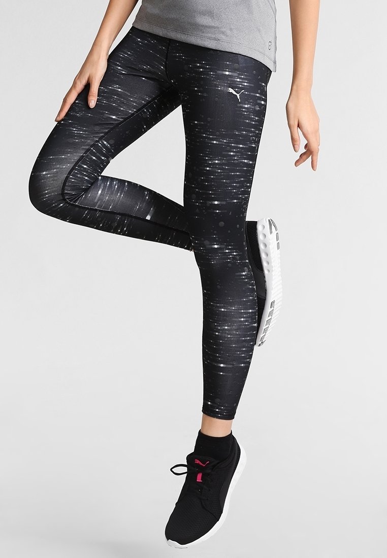 Mustat legginssit, joissa on teksturoitu kuvio valkoisista pystysuorista viivoista, tiukka malli ja Puma-logo yläreidessä. Yhdistetty mustiin kenkiin.