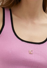 Růžový žebrovaný top s černým lemem, se malým zlatým logem "LC" uprostřed. Měkká textura, přiléhavý design a vertikální pruhy.