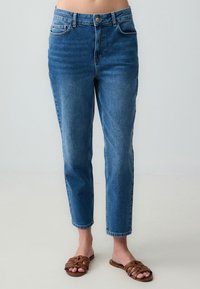 Jeans in denim a vita alta di blu medio, con gamba dritta, cinque tasche, lievi sfumature e chiusura a bottone metallico.
