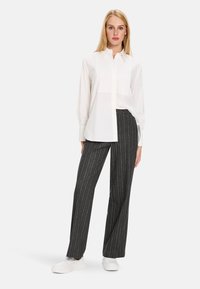 White button-down shirt with long sleeves, paired with dark gray pinstripe trousers and white slip-on shoes. Simple, tailored design.