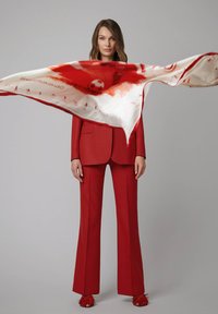 Czerwony elegancki garnitur z rozszerzanymi spodniami, połączony z jedwabnym szalem w wzory z motywem piłkarskim oraz czerwonymi butami z frędzlami.