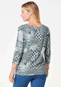 Musterbluse mit Dreiviertelärmeln, die blaue und grüne geometrische Designs aufweist, aus leichtem Stoff und mit rundem Ausschnitt.