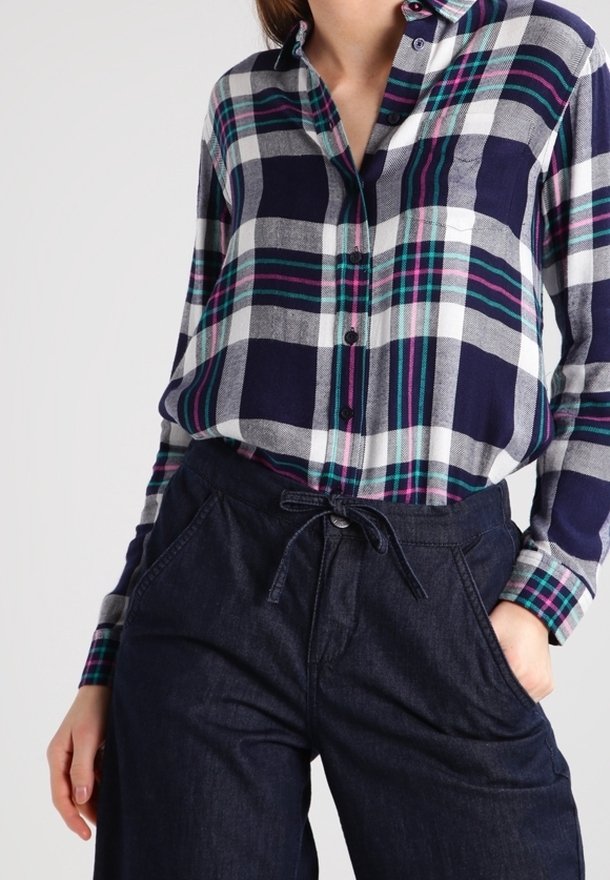 Chemise en flanelle à carreaux bleu marine et blanc avec des rayures vertes et roses, design boutonné, associée à un pantalon en denim foncé avec une taille à cordon.