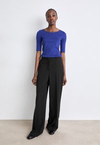 Koninklijkblauw aansluitend topje met korte mouwen, gecombineerd met hoge zwarte pinstripe broek. Gladde textuur en rechte snit.