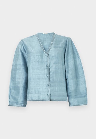 Φωτεινό μπλε μπλούζα με μακριά μανίκια από υφή υφάσματος, στρογγυλή λαιμόκοψη, κλείσιμο με κουμπιά μπροστά και λευκή ραφή κατά μήκος των άκρων.