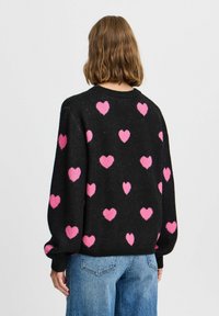 Maglione nero con scollo rotondo, decorato con motivi a cuore rosa. Maniche lunghe a palloncino e orlo a coste.