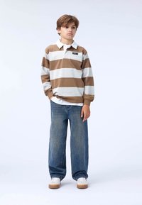 Striped long-sleeve polo in brown and white, with a white collar. Paired with loose-fit blue jeans and white sneakers. No visible patterns.