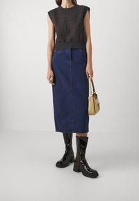 Mørk stribet ærmeløs sweater, højlivede blå denimskørt, glansfulde sorte knæhøje støvler, lille gul taske med krokodilleskindspræg.