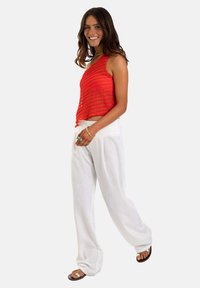 Top rojo sin mangas con rayas horizontales texturizadas, combinado con pantalones de lino blancos sueltos y sandalias marrones.