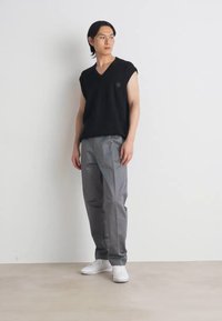 Svart ärmlös topp med V-ringning, kombinerad med ljusgrå byxor och vita sneakers. Slät textil, avslappnad passform, minimalistisk design.