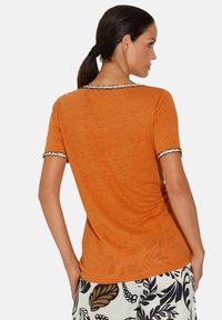 Korte mouwen, oranje T-shirt met een textuurafwerking, voorzien van een zwart-wit golvende kraag en manchetten. Geschikt voor casual draag.