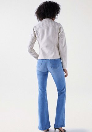 Lys grå læderjakke med kviltede skulderdetaljer, parret med blå kløverjeans. Glat tekstur og tætsiddende design.