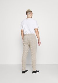 Beige mönstrade byxor med elastisk midja, med ett rutmönster och kontrasterande randiga sidpaneler, i kombination med svarta sneakers.