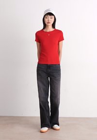 Camiseta roja de manga corta con escote redondo, combinada con jeans oscuros de pierna ancha y zapatillas blancas con suelas marrón claro.