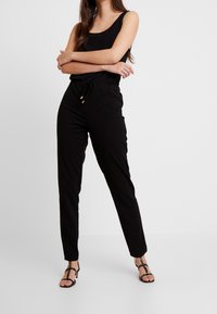 Mono negro con escote en pico, cintura con cordón y perneras ajustadas. Fabricado en material suave, con un diseño minimalista y sin patrones.