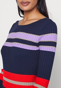 Maglione a righe blu Navy, con bande orizzontali di rosso, viola e beige. Collo a giro e tessuto a maglia testurizzato.