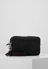 Zwarte nylon tas met ritssluiting, voorzien van een rond logo, een kleine aap hangertje en een afneembare bruine band voor gemakkelijk dragen.