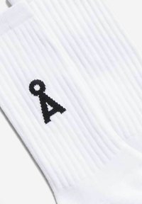 Weiße Baumwollsocken mit geripptem Muster, mit einem schwarzen bestickten Logo an der Seite, das wie eine Kombination aus einem Kreis und einem "A" aussieht.