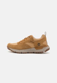 Zapatilla de ante y malla en tono tostado con acentos beige y suela de goma robusta. Presenta cordones redondos y un logo en el costado, diseñada para ofrecer durabilidad.