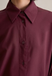Burgundy long-sleeve shirt featuring a classic collar, front button closure, and smooth, lightweight fabric texture.
