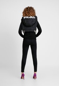 Svart kort puffjacka med huva, med stor vit logo och accentpatchar, tillsammans med svarta skinny jeans och lila klackar.