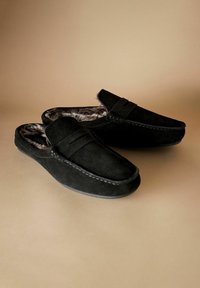 Juodos suede mokasinų šlepetės su minkšta dirbtinės vilnos pamušalu, plokščiu padu, siuvinėjimu ir juostelės akcentu viršuje.