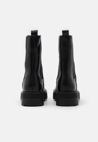 Botas de tobillo negras hechas de cuero liso, con caña alta, tacón rectangular y tiradores en la parte trasera.