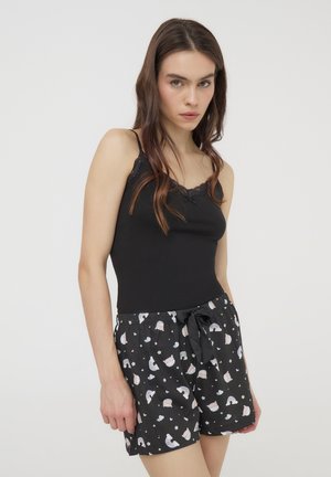 Camisole nera con rifiniture in pizzo, abbinata a pantaloni corti neri con motivi colorati di arcobaleni e nuvole. Design comodo e dal fit largo.
