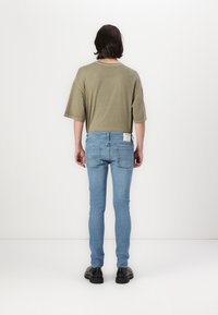Maslinasto zelena oversized majica, uparena s svijetloplavim skinny trapericama. Traperice imaju mali oznaku na zadnjem džepu i nosi ih s crnim cipelama.