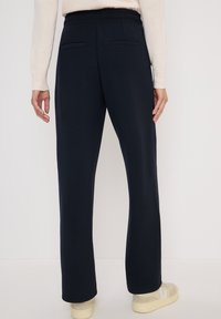 Marineblauwe joggingsbroek met een zachte textuur, elastische tailleband, twee achterzakken en een relaxed fit, gecombineerd met lichtgekleurde sneakers.
