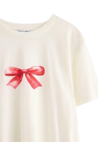 Kremowa koszulka wykonana z miękkiej bawełny. Posiada czerwony akwarelowy wzór w kształcie kokardy z przodu, krótkie rękawy i okrągły dekolt.