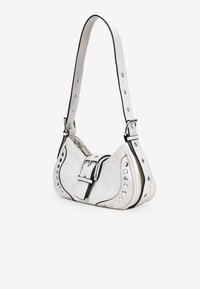 Bolso de mano de cuero blanco con acentos de tachuelas plateadas, detalle de hebilla y un ribete negro en contraste. Cuenta con una correa de hombro y cierre de cremallera.