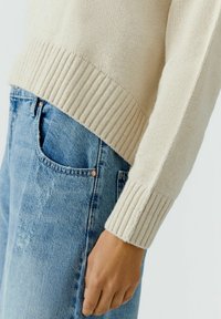 Crème rib gebreide trui met een textuurafwerking, gecombineerd met lichtblauwe versleten jeans, met zichtbare zakdetails en een aansluitende silhouet.