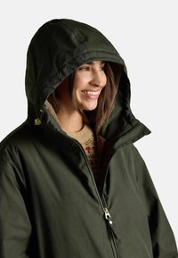 Oliven grøn udendørsjakke med hætte, lynlåslukning og blødt indvendigt foer. Har fremtrædende syninger og hardware-detaljer.