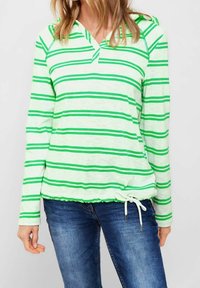 Zielona i biała w paski bluza z długim rękawem i dekoltem w serek, z ściągaczem na dole, wykonana z lekkiego materiału, zestawiona z dżinsami.