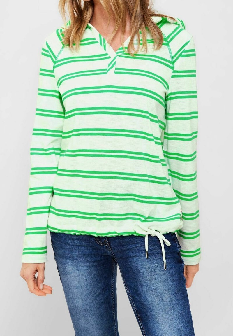 Zielona i biała w paski bluza z długim rękawem i dekoltem w serek, z ściągaczem na dole, wykonana z lekkiego materiału, zestawiona z dżinsami.