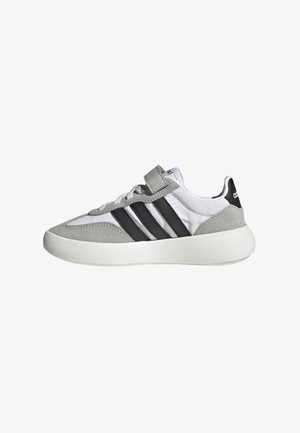 Zapatilla gris y blanca con parte superior de ante texturizado y sintético suave, que presenta tres franjas negras, un cierre de cordones y un cuello acolchado.