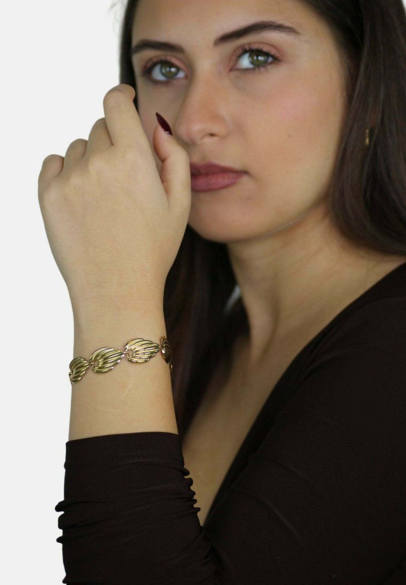 Bracciale in metallo dorato con link a forma di foglia e finitura lucida, indossato su un polso con una manica scura, su uno sfondo chiaro.