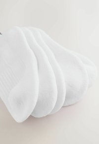 Fünf gefaltete weiße Knöchelsocken, auf einem hellen Untergrund gestapelt, mit einem leichten Schatten auf der linken Seite.