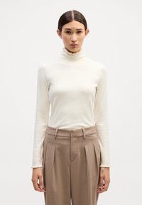 Langærmet turtleneck-top i off-white ribbet stof med en flagrende krave og slim fit. Sammen med høj talje, beige bukser.